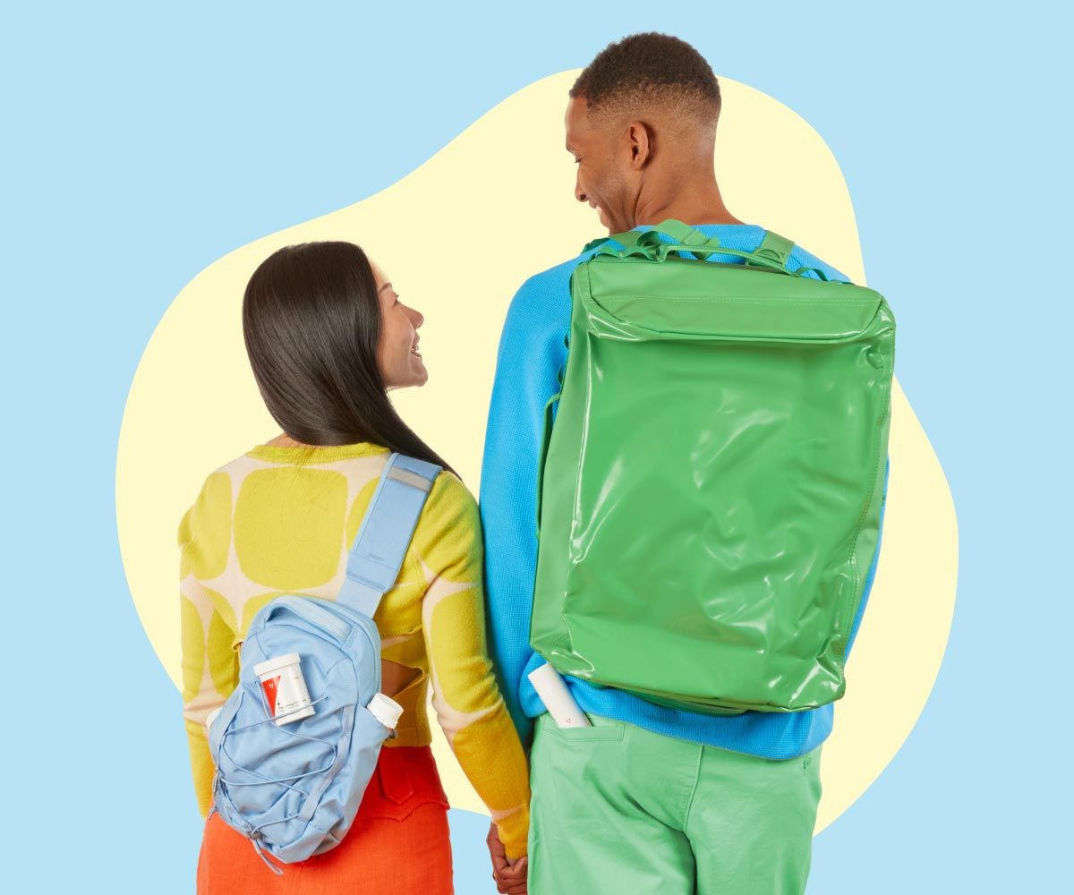 A man and woman are wearing bright colorful clothing while holding hands and smiling at each other while in front of a light blue background