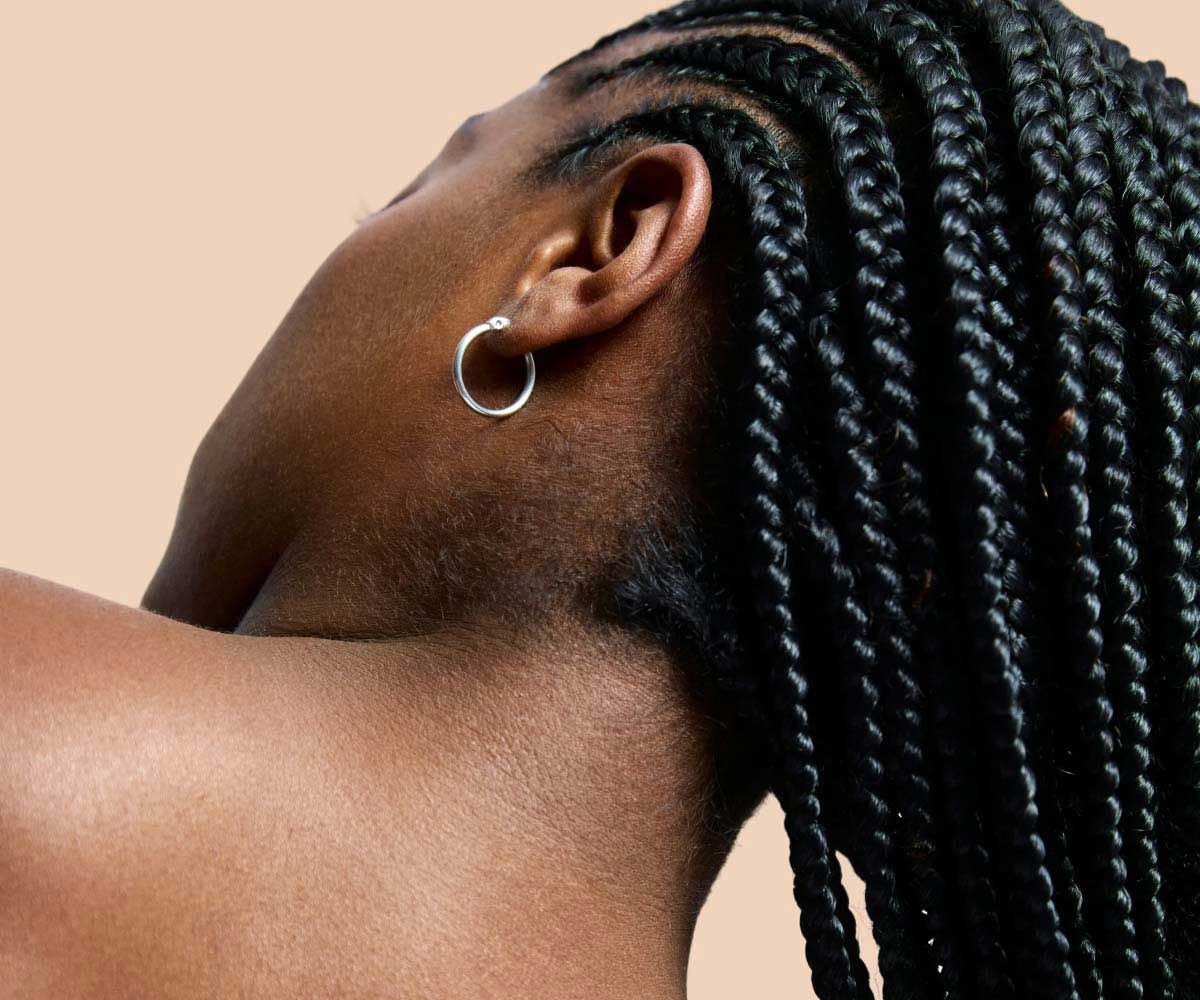 A close up of a woman's neck and shoulders with clear skin in front of a cream background