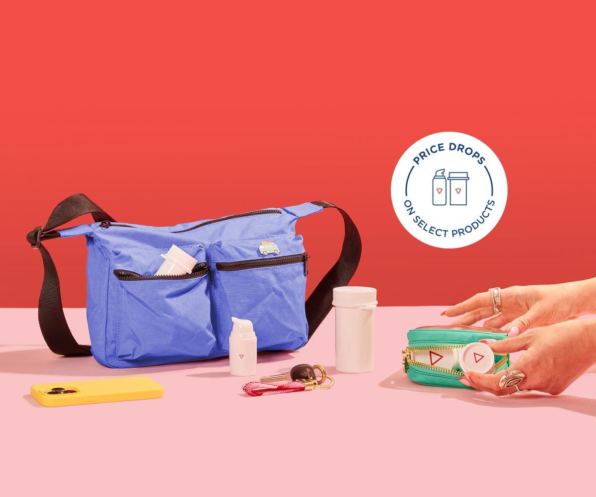 A woman's hands grabbing Wisp medication vials from a travel pouch sitting on a pink surface with a mobile phone, keys and a larger travel bag