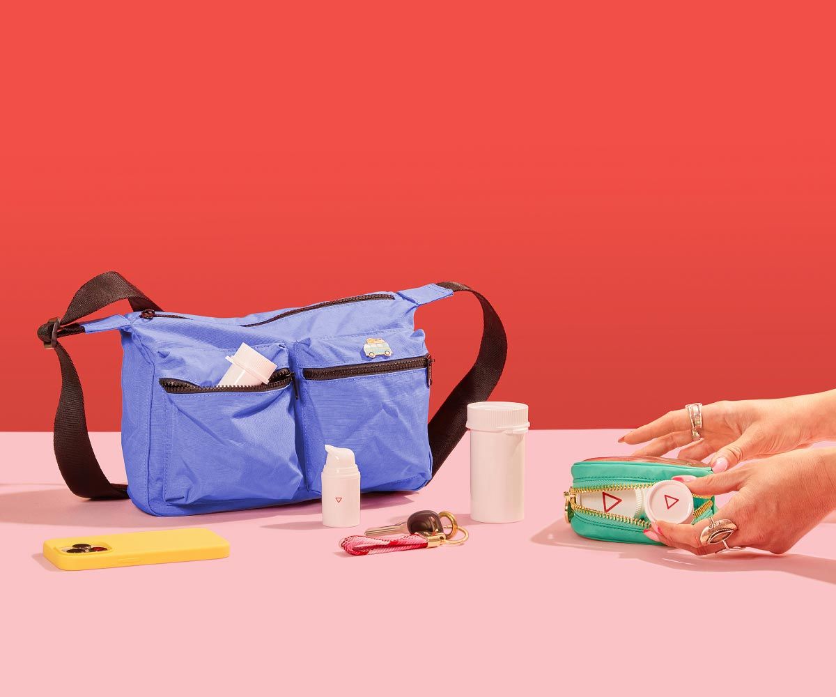 Various Wisp products on a pink surface with a blue travel back and a green travel pouch, a yellow mobile phone and keys on a pink surface with a red background