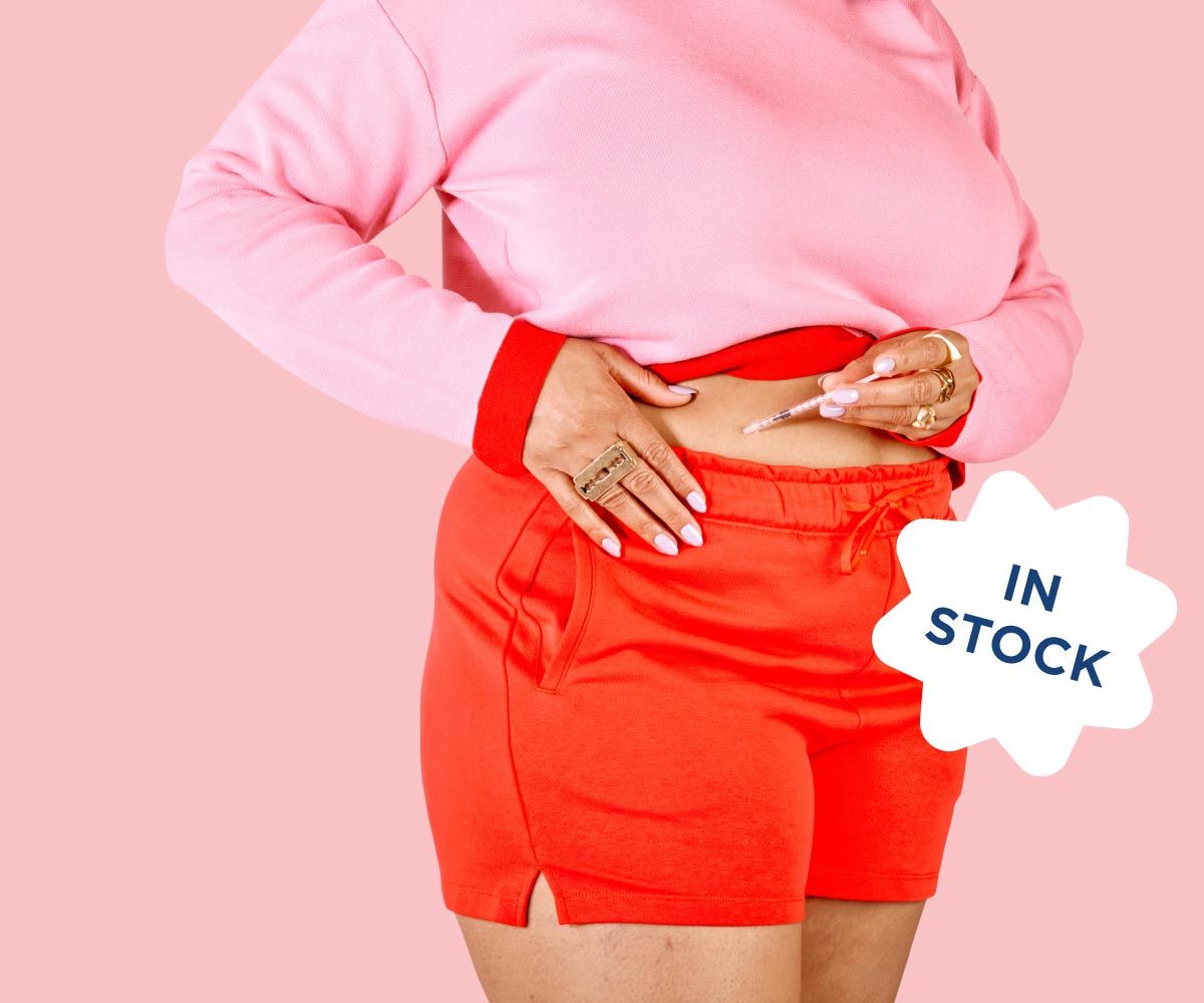 A woman wearing red shorts and a pink sweater injects GLP-1 weight loss medication to her stomach
