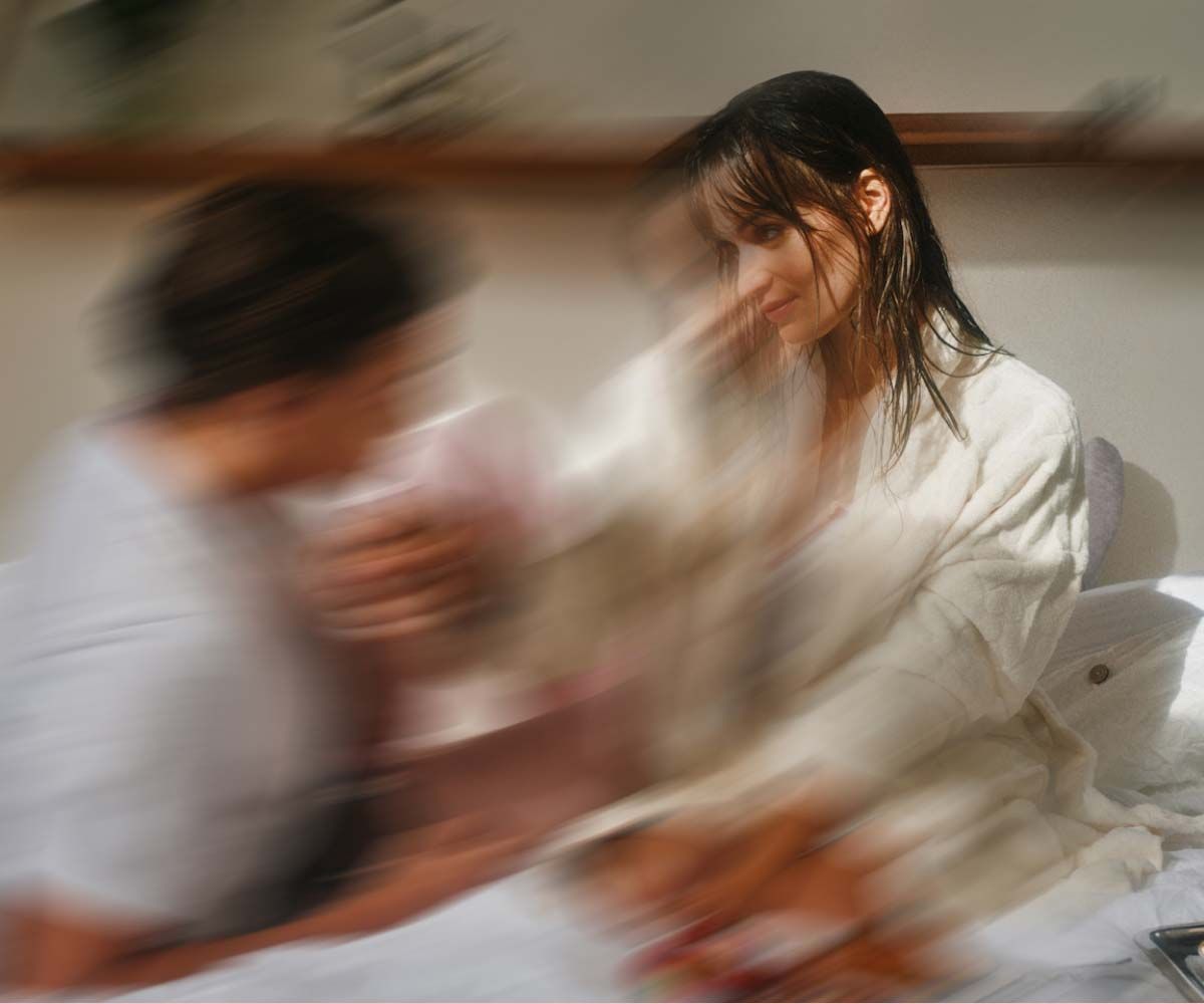A man and woman sitting on a bed looking at each other with motion blur