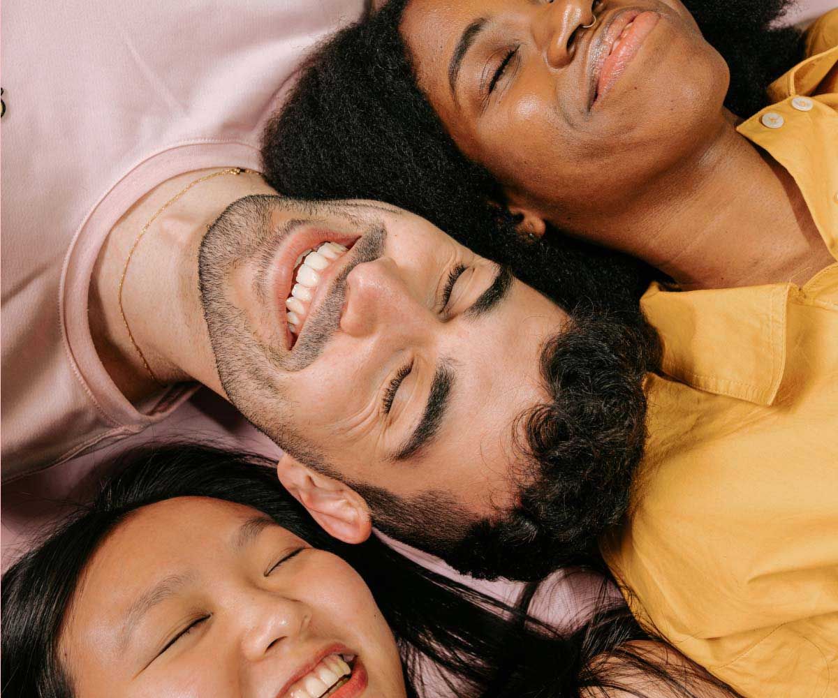 Two women and a man wearing colorful clothes while laying on their back and smiling