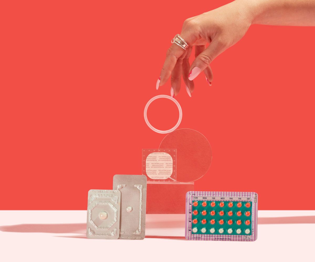 2 Emergency Contraception packets and a birth control packet, ring, and patch are balanced on a clear block on a pink surface with a red background