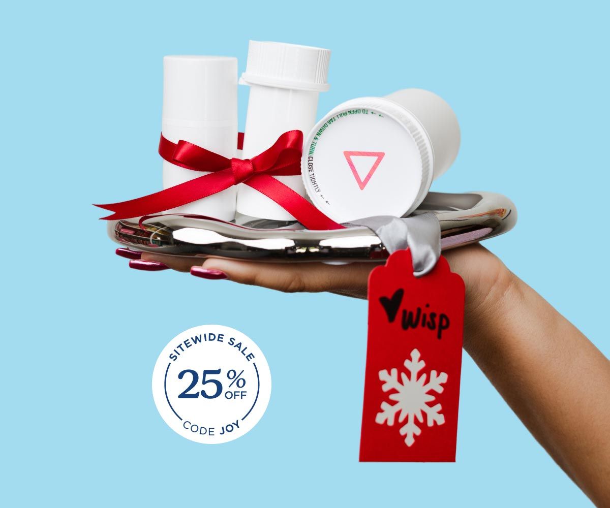 A woman's hand holding a silver tray with multiple Wisp pill vials with a red ribbon around them in front of a light blue background