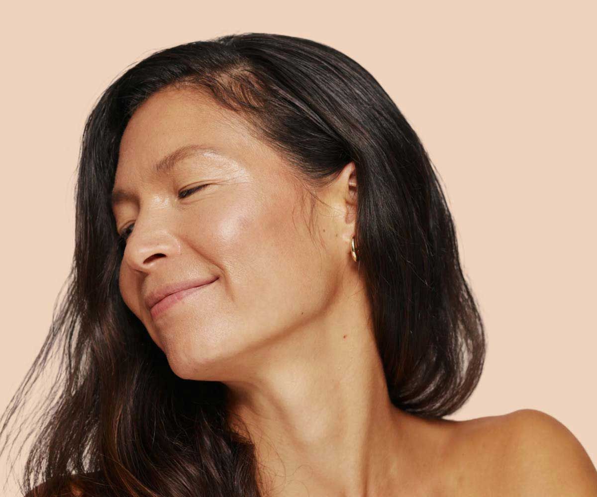 A smiling woman with glowing skin and dark hair with a cream background