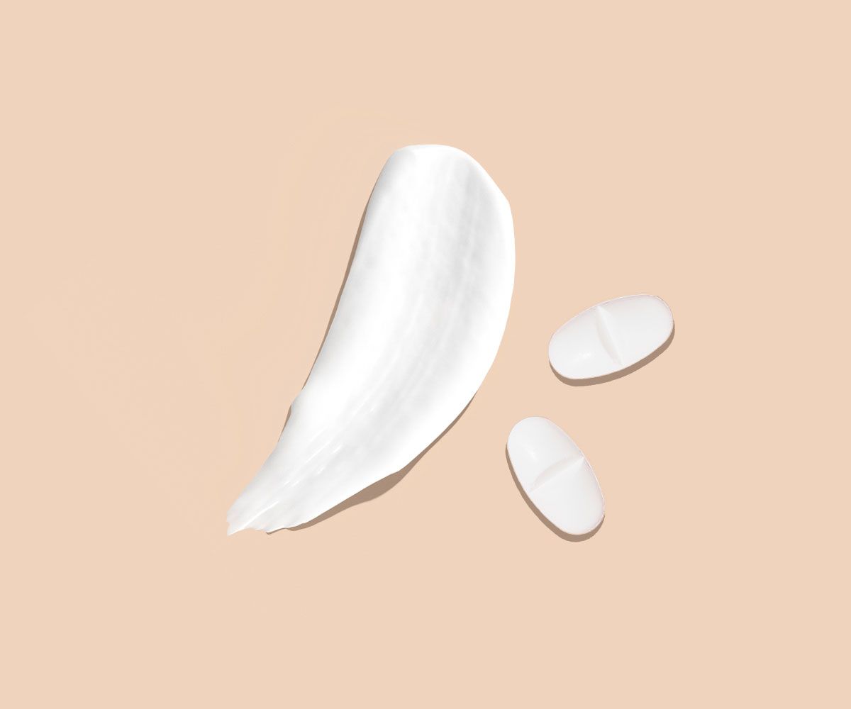 A cream swatch and two white pills on a cream surface