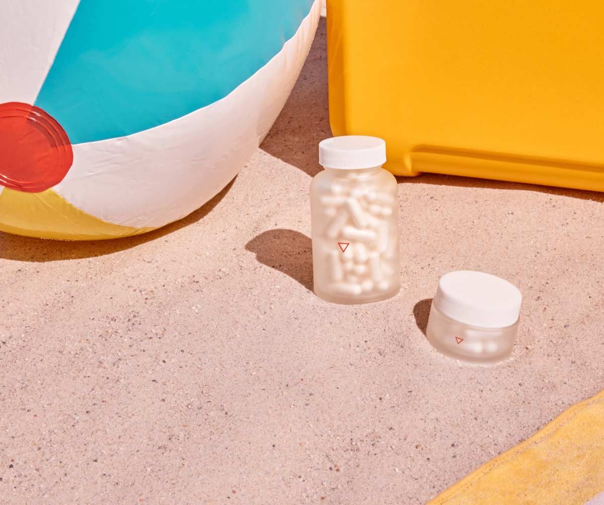 Two Wisp glass pill jars on beach sand next to a beach ball and chair