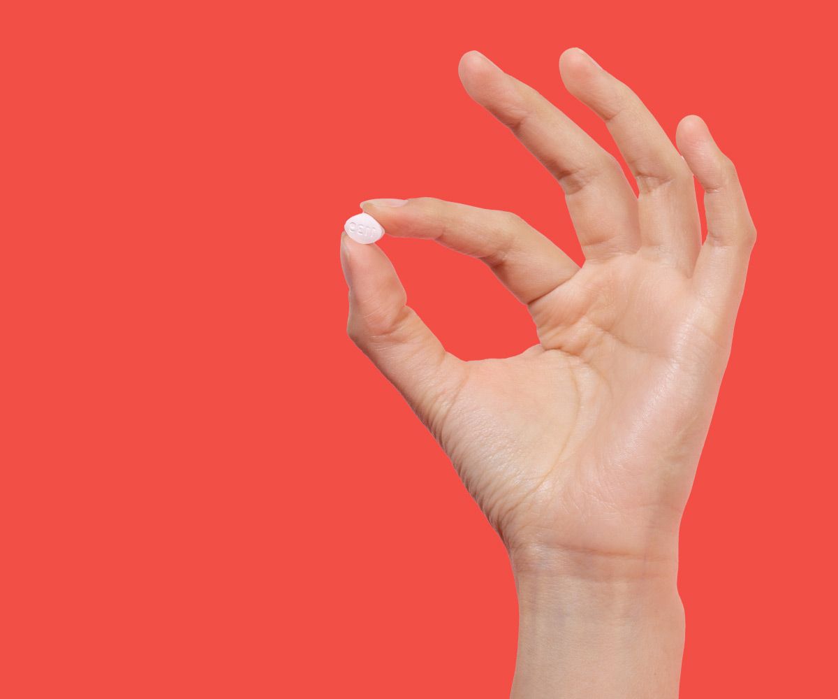 Hand holding fluconazole pill for same-day yeast infection treatment on a red background