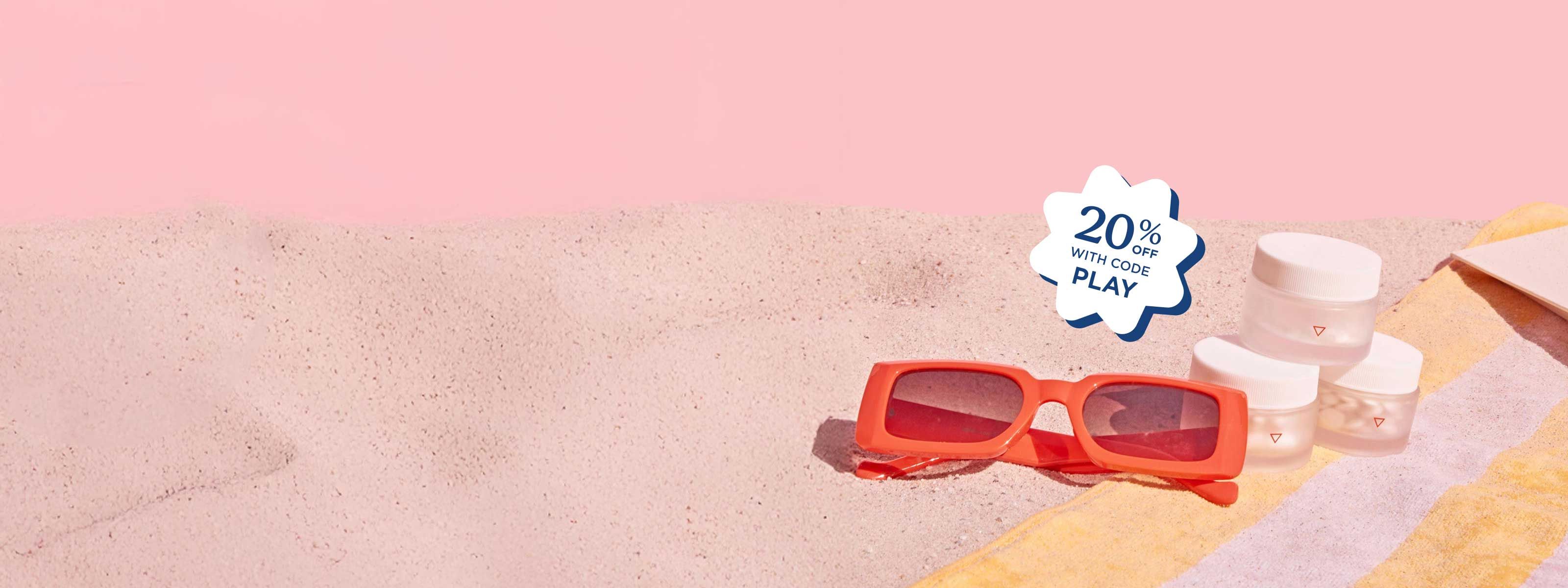 3 stacked Wisp jars and red sunglasses on a pink and yellow striped beach towel on sand