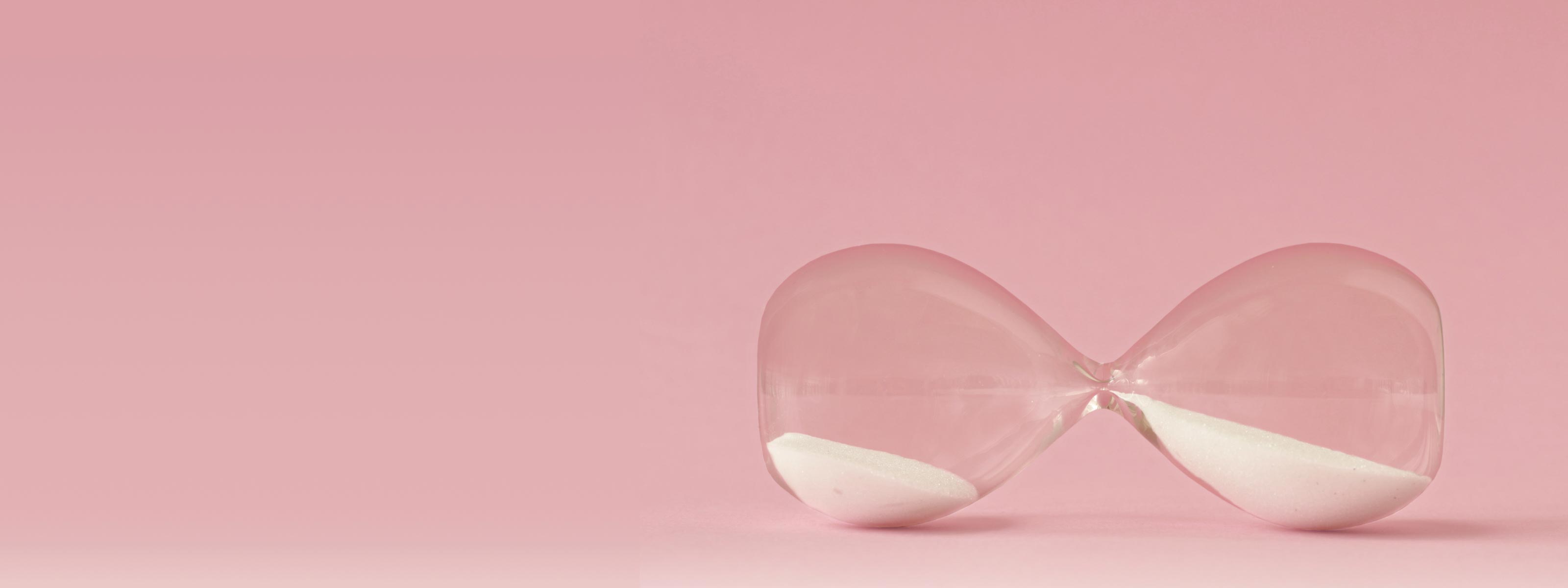 An hourglass laying on it's side on a pink surface