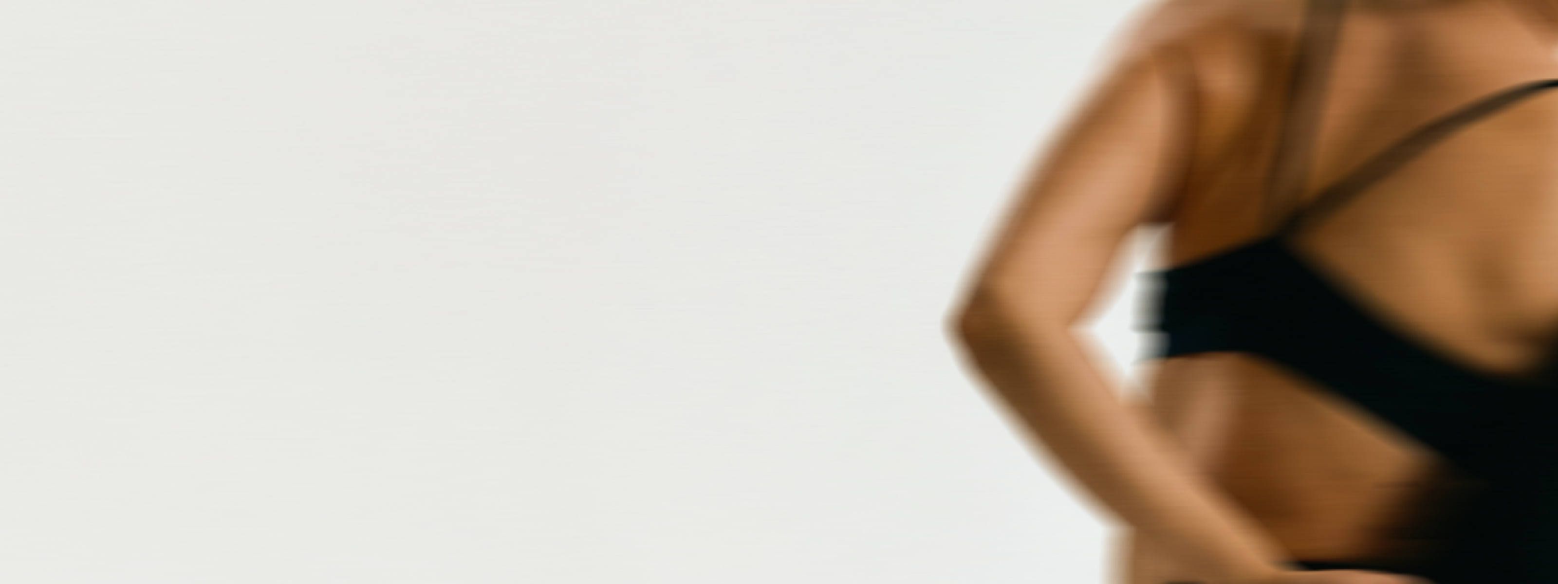 Blurred close-up of a woman's torso and arm, hand resting on her hip, wearing a black sports bra — desktop banner image for content on menopause and joint pain.
