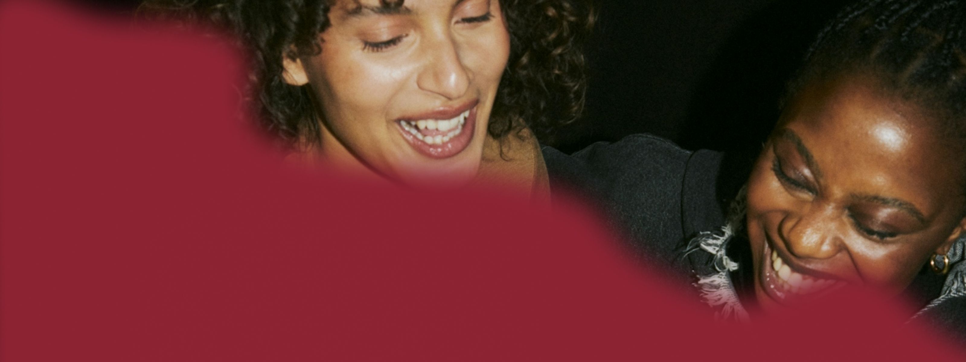 two women laughing with a dark red overlay of color over half the image