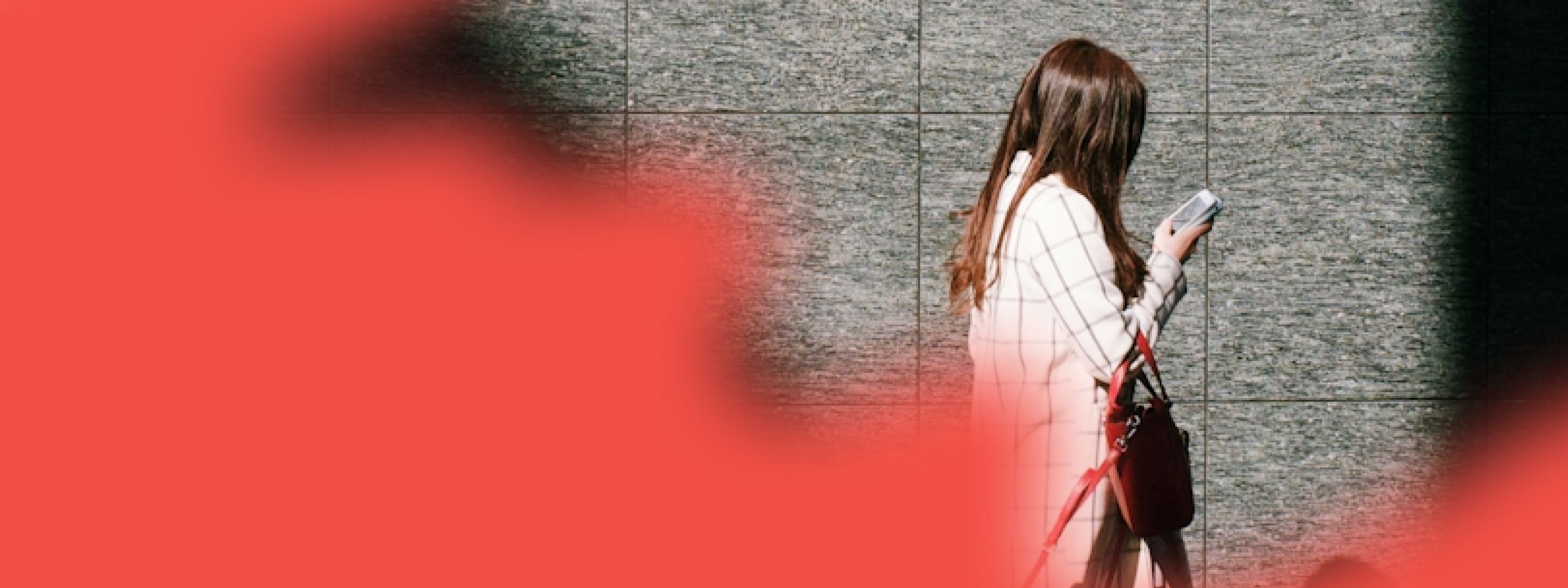 A woman walking with her head down while looking at her phone and a red overlay of color on half of the image