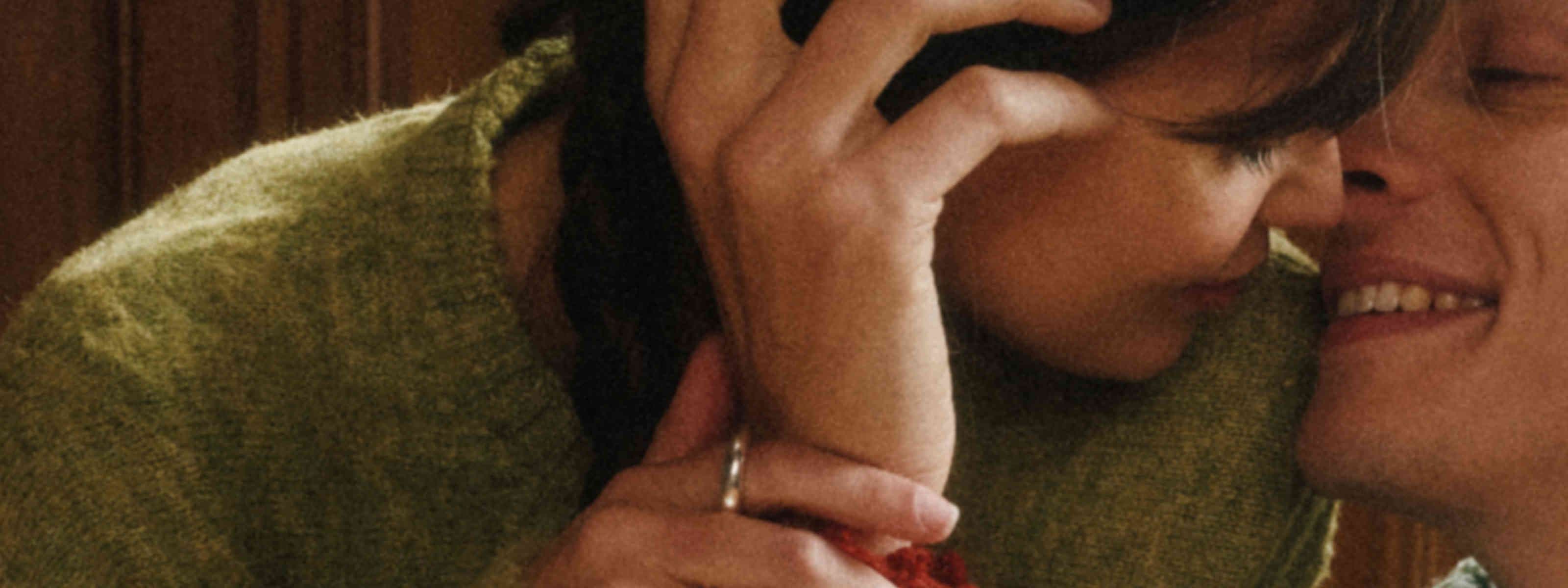 image of woman affectionately embracing a smiling man, nuzzling his cheek, in a warm, softly lit setting