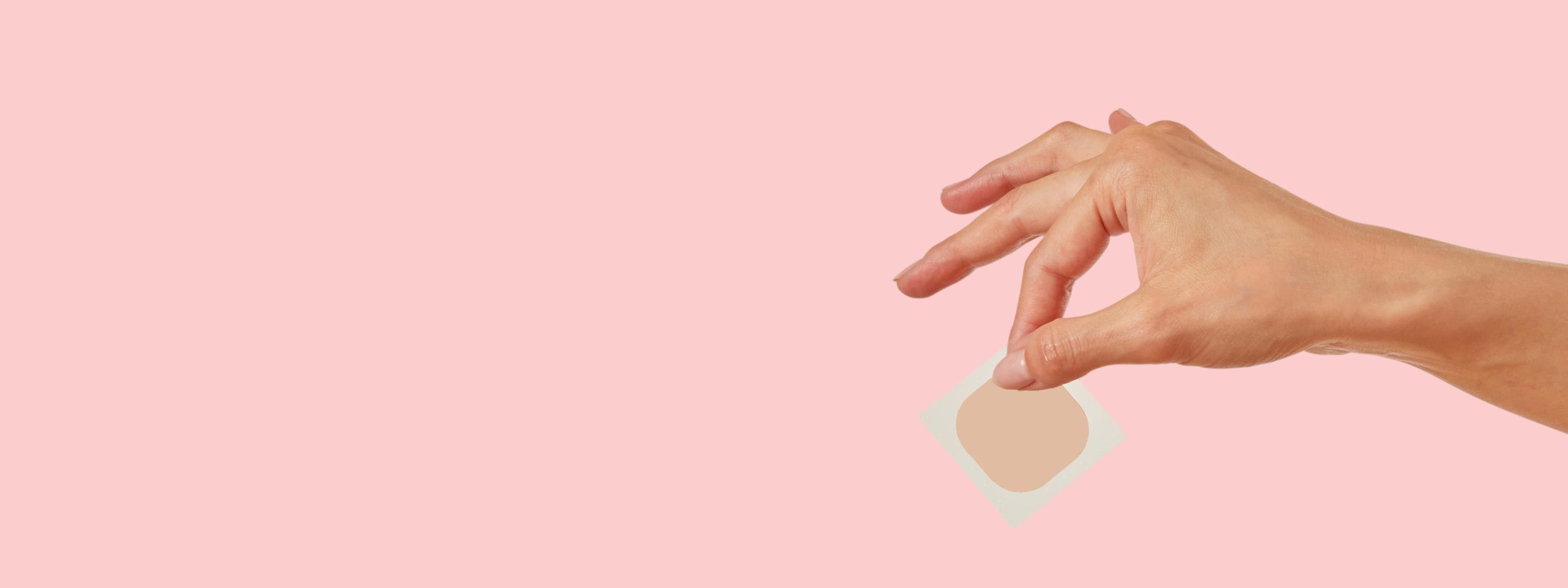 A woman's hand holding a Wisp medication patch with a pink background