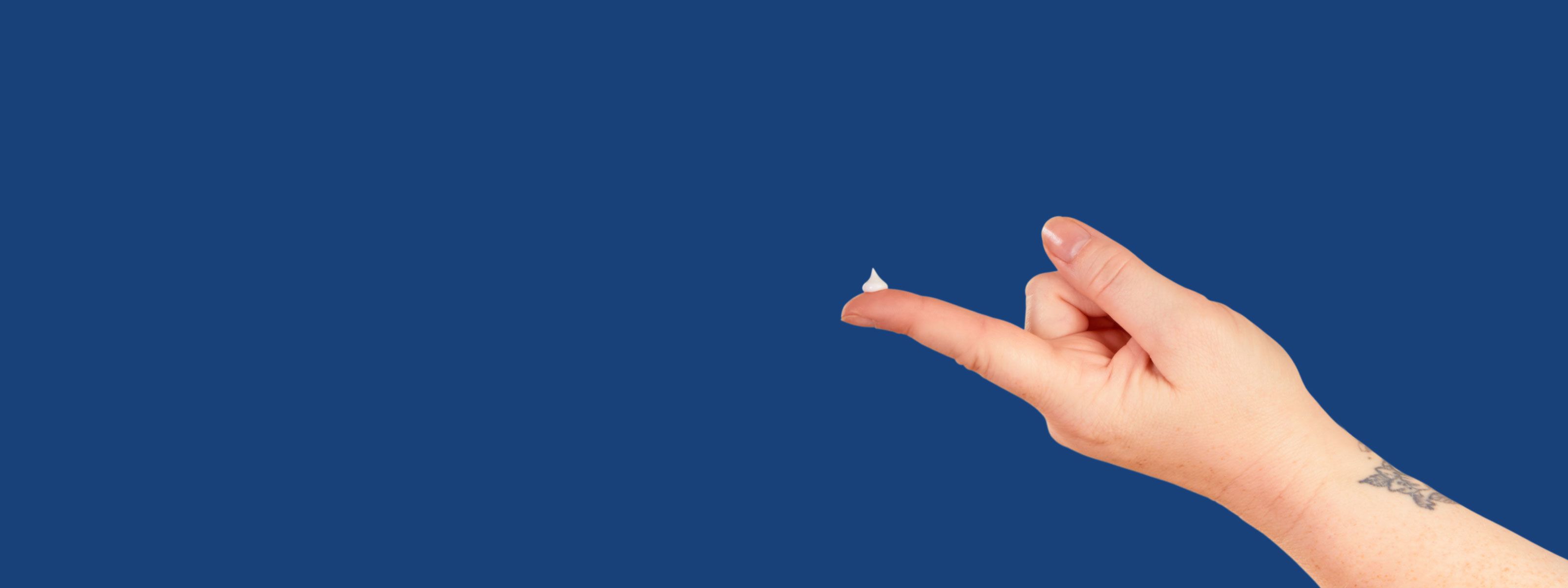 A hand with hemorrhoid treatment on the fingertip on a dark blue background