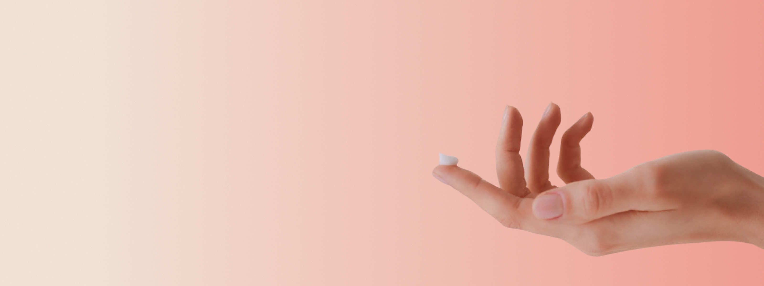 hand holding a dose of clotrimazole cream in front of a light orange and beige background