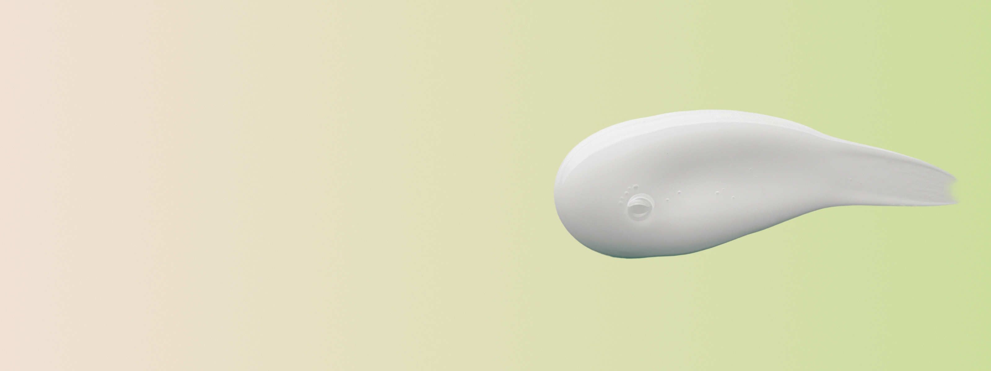 swipe of white cream in front of a green and beige background