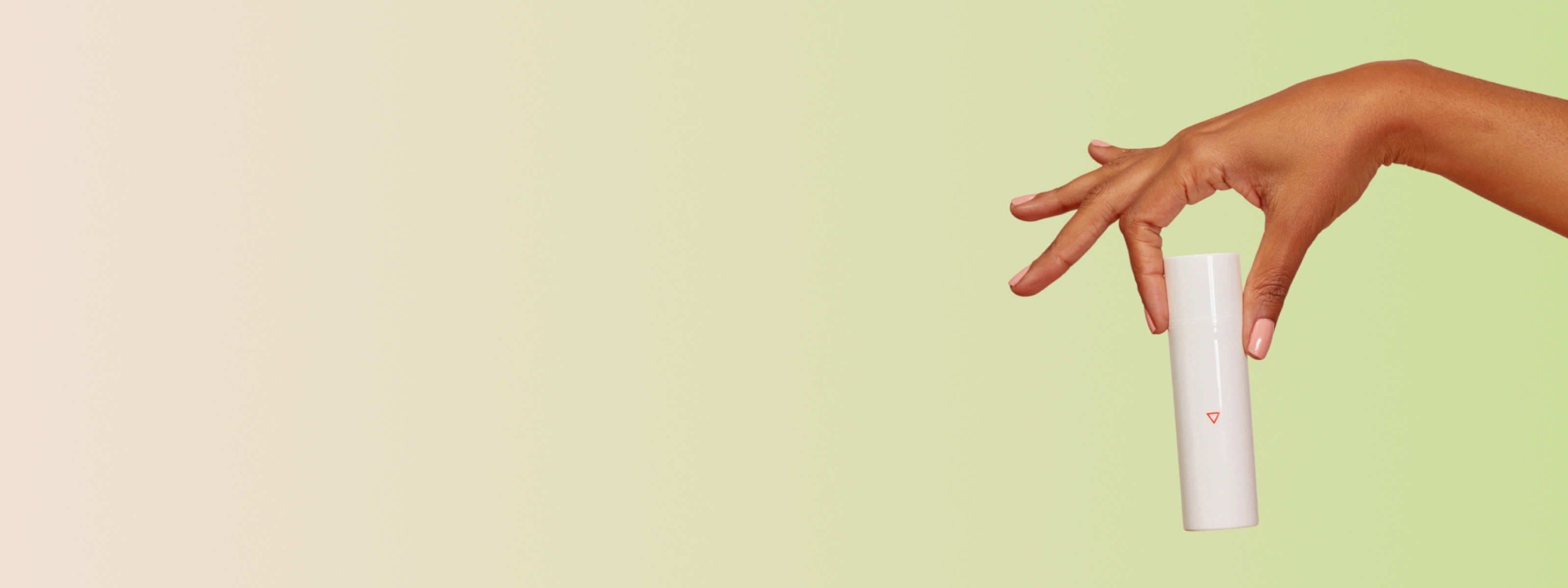 A woman's hand holding a Wisp skincare bottle with a pink background