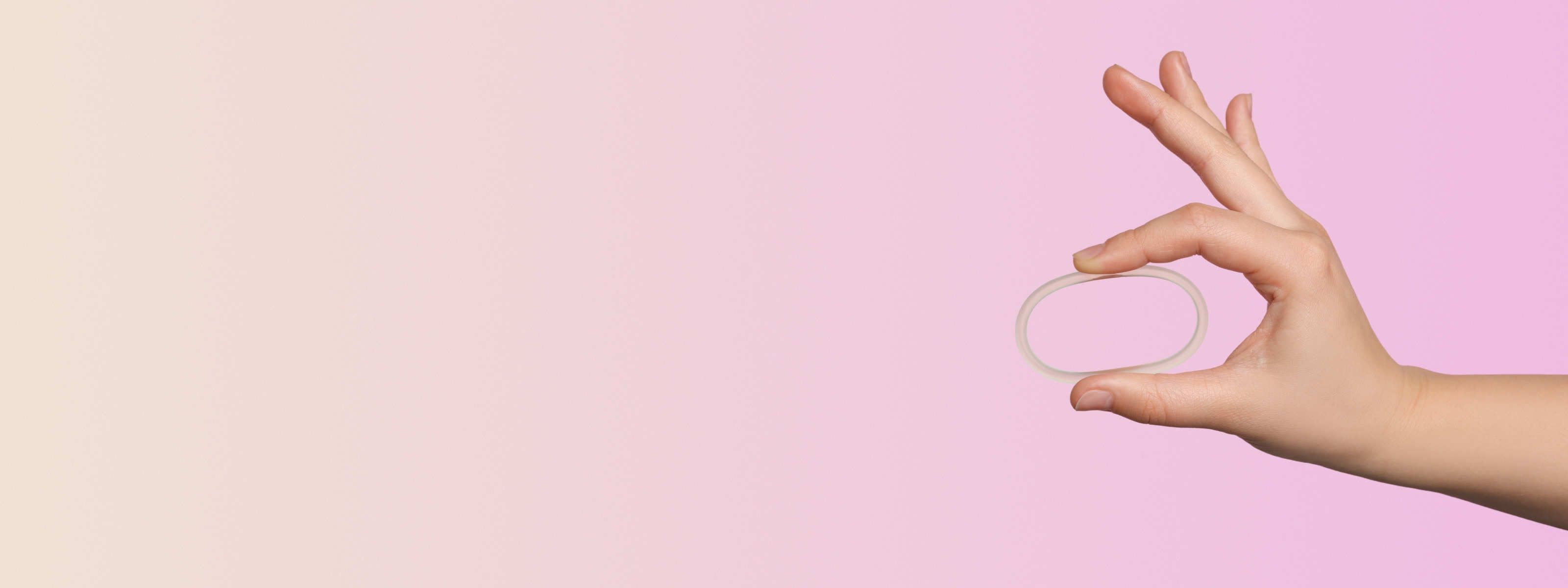 Woman's hand holding NuvaRing Birth Control with a pink background
