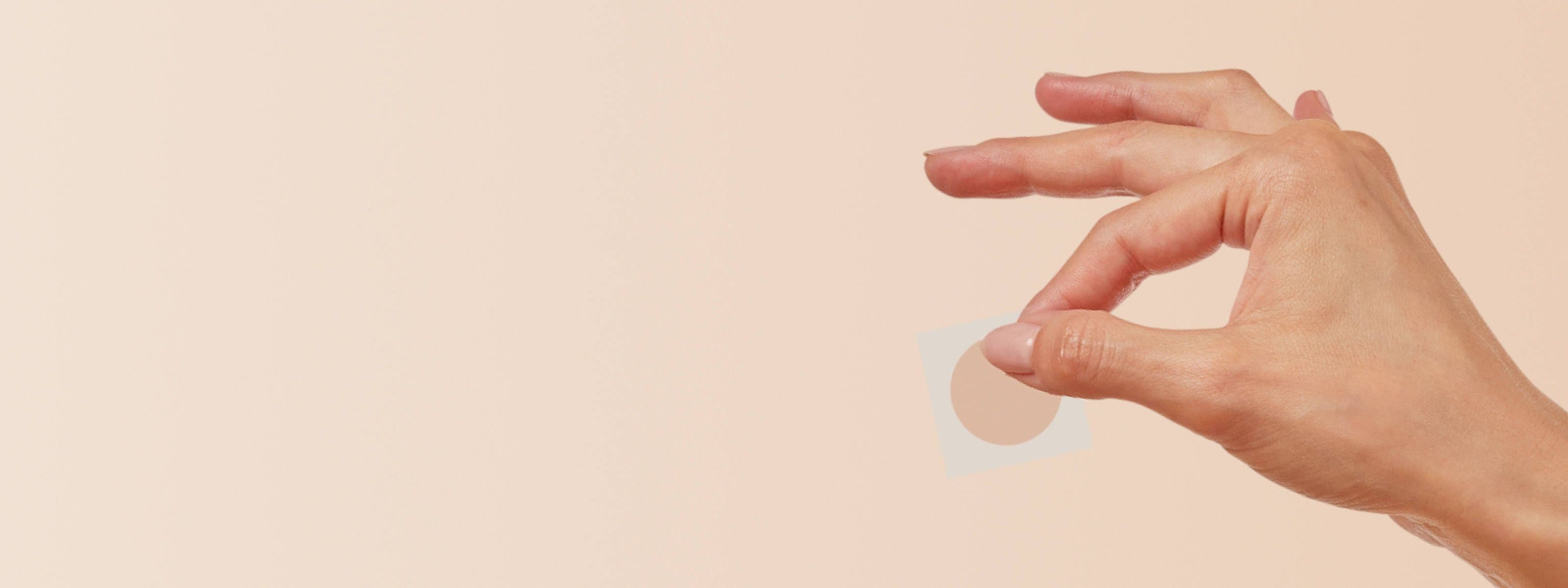 hand holding a scopolamine patch in front of a beige background