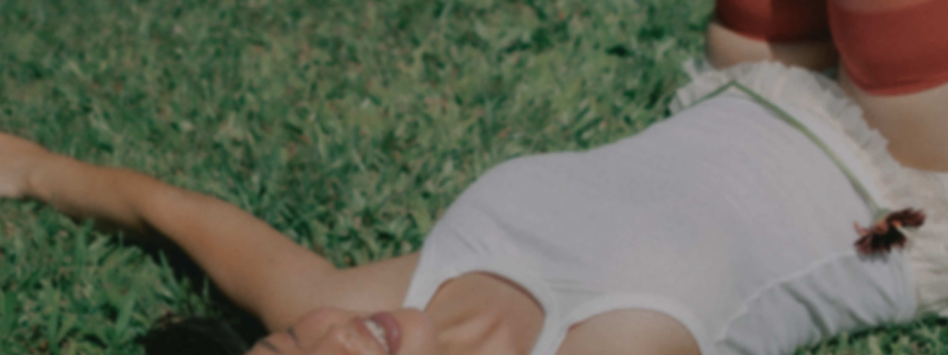 Woman lying relaxed in grass with eyes closed, smiling peacefully, representing relief and comfort while managing a UTI.
