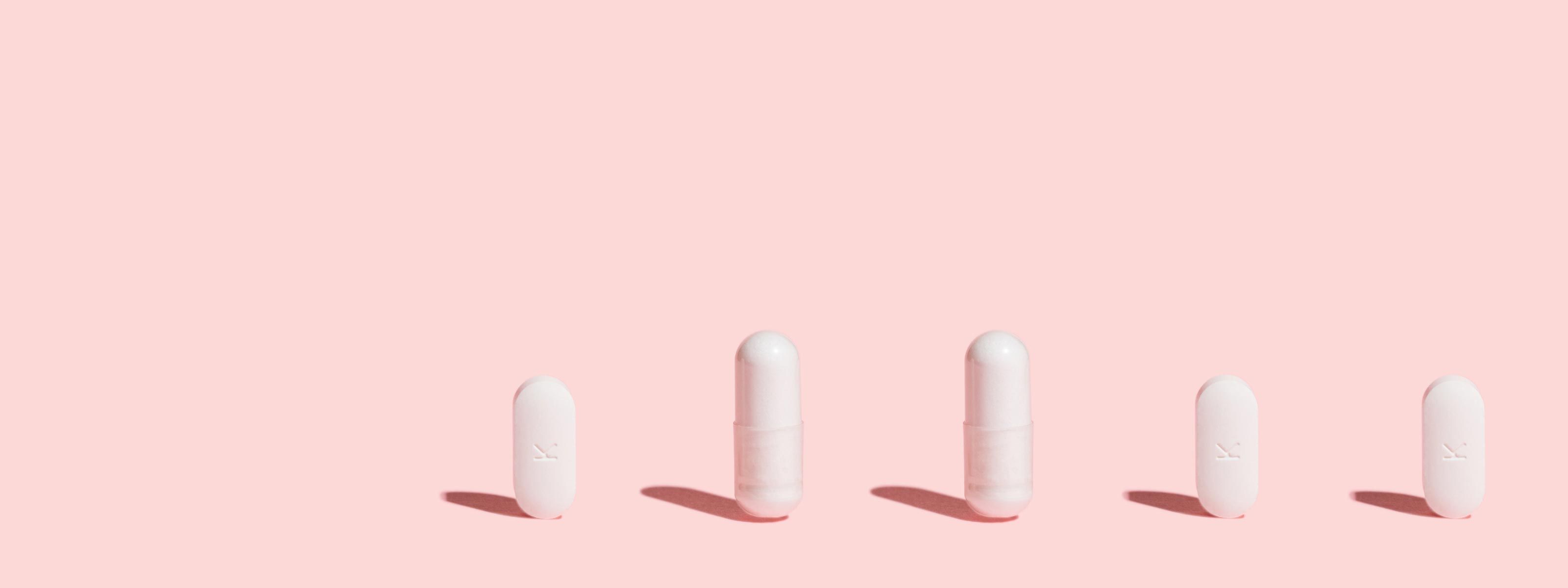 Clindamycin and other antibiotics pills balanced on a pink surface