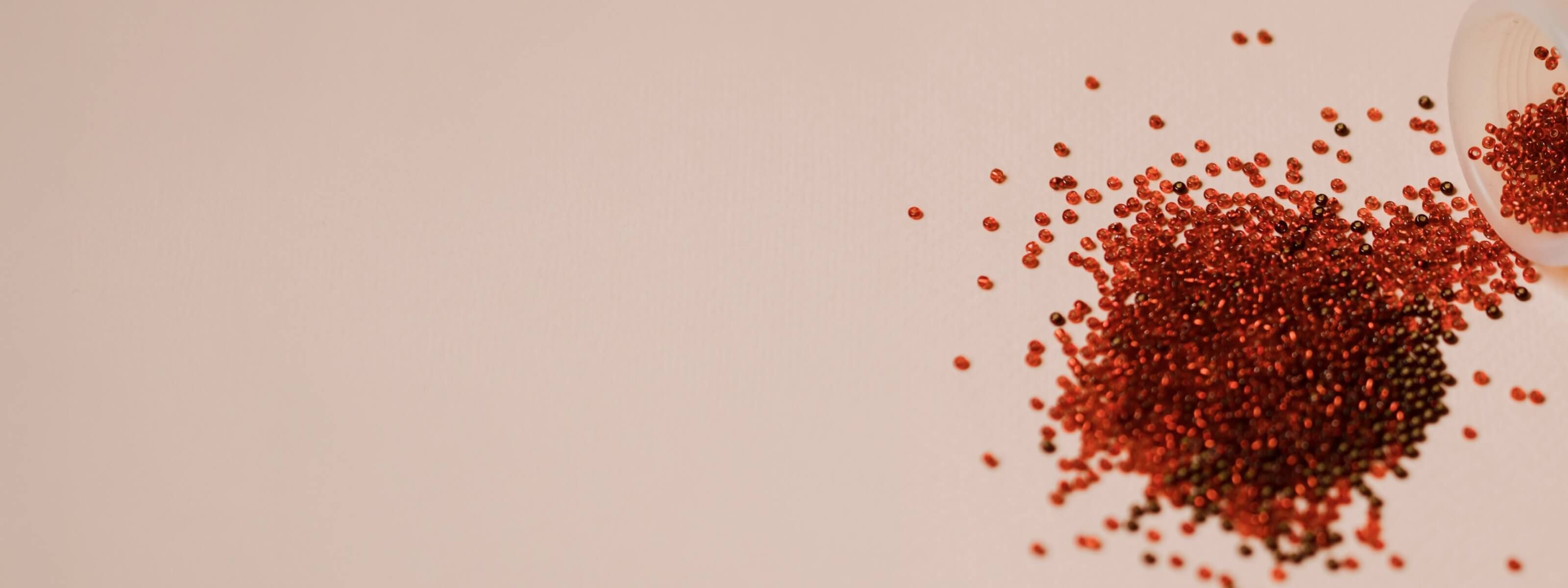 beige background with a spilled cup of small red beads creating a pile