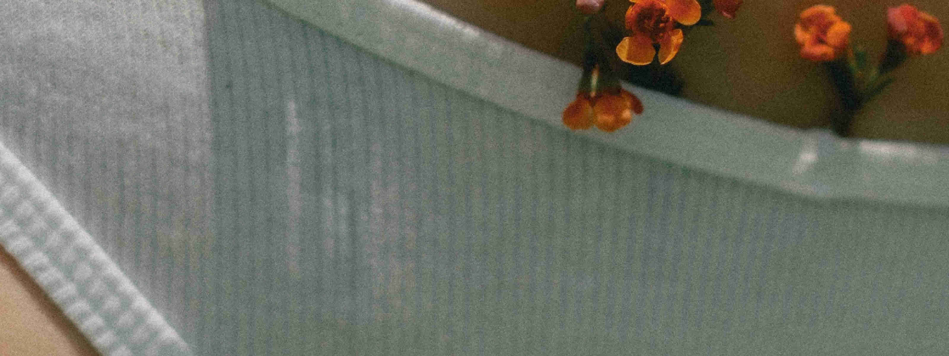 Close-up, textured photo of pale sage-green underwear with a ribbed texture. Orange and rust-colored marigold flowers with green stems emerge from the top edge, set against a warm tan background.