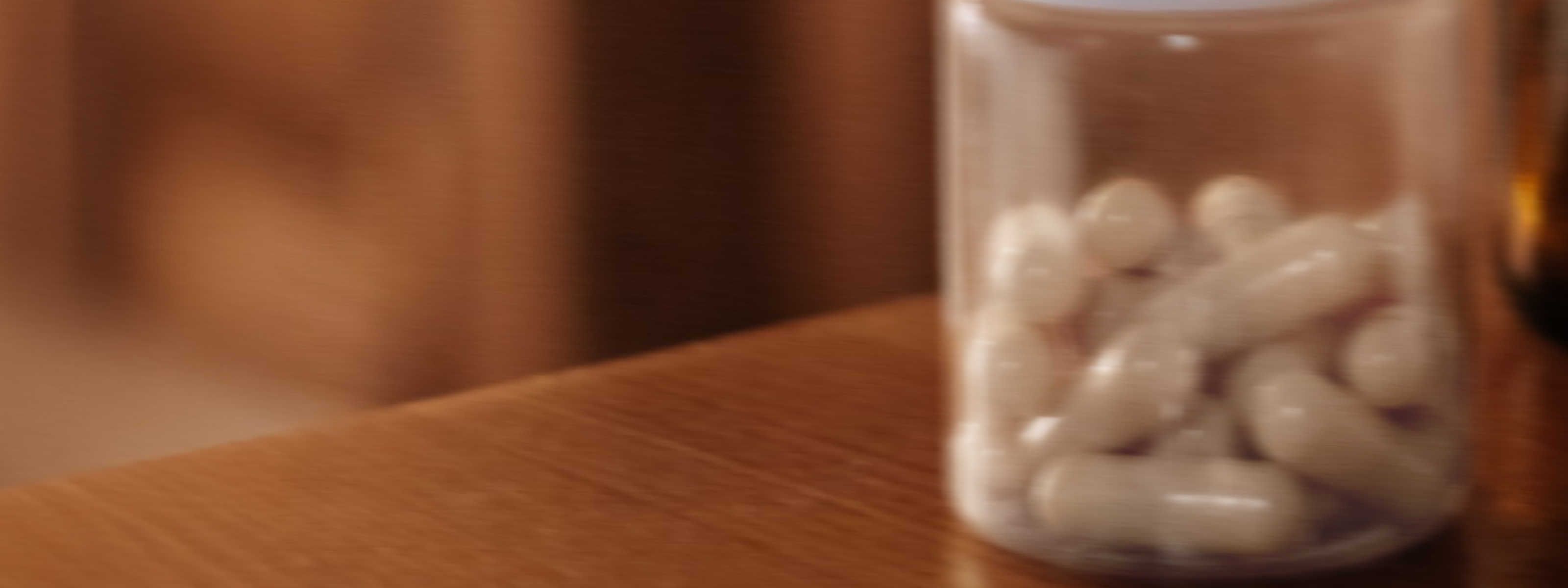 image of a clear, blurry bottle with white capsules on a brown wooden desk