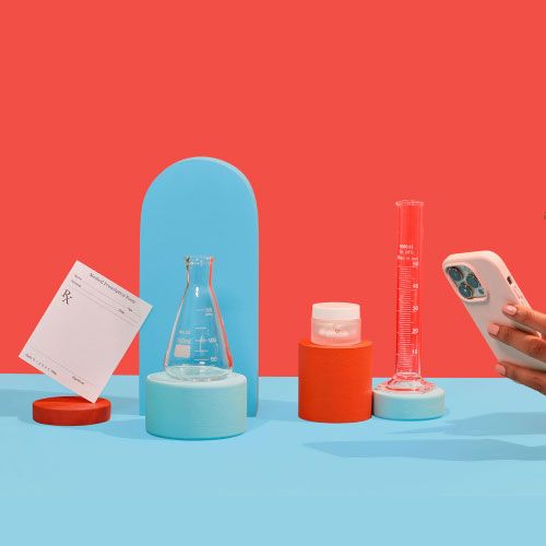 A woman holding a mobile phone next to test tubes and a Wisp glass pill jar balanced on colorful abstract shapes