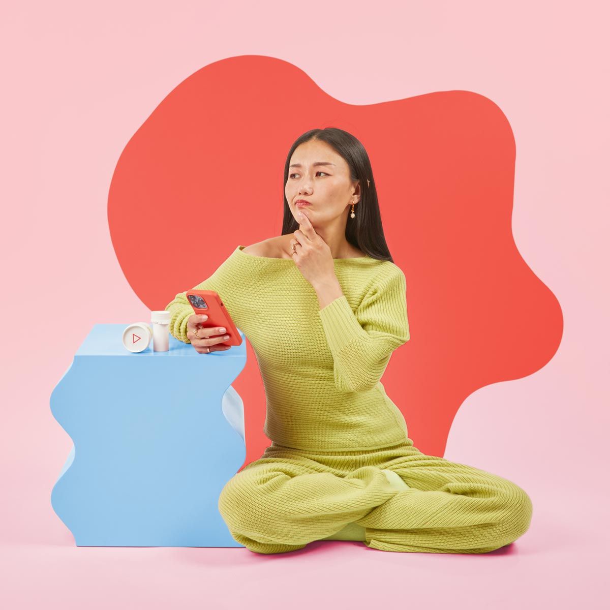 A confused woman holds her phone in front of a colorful geometric background