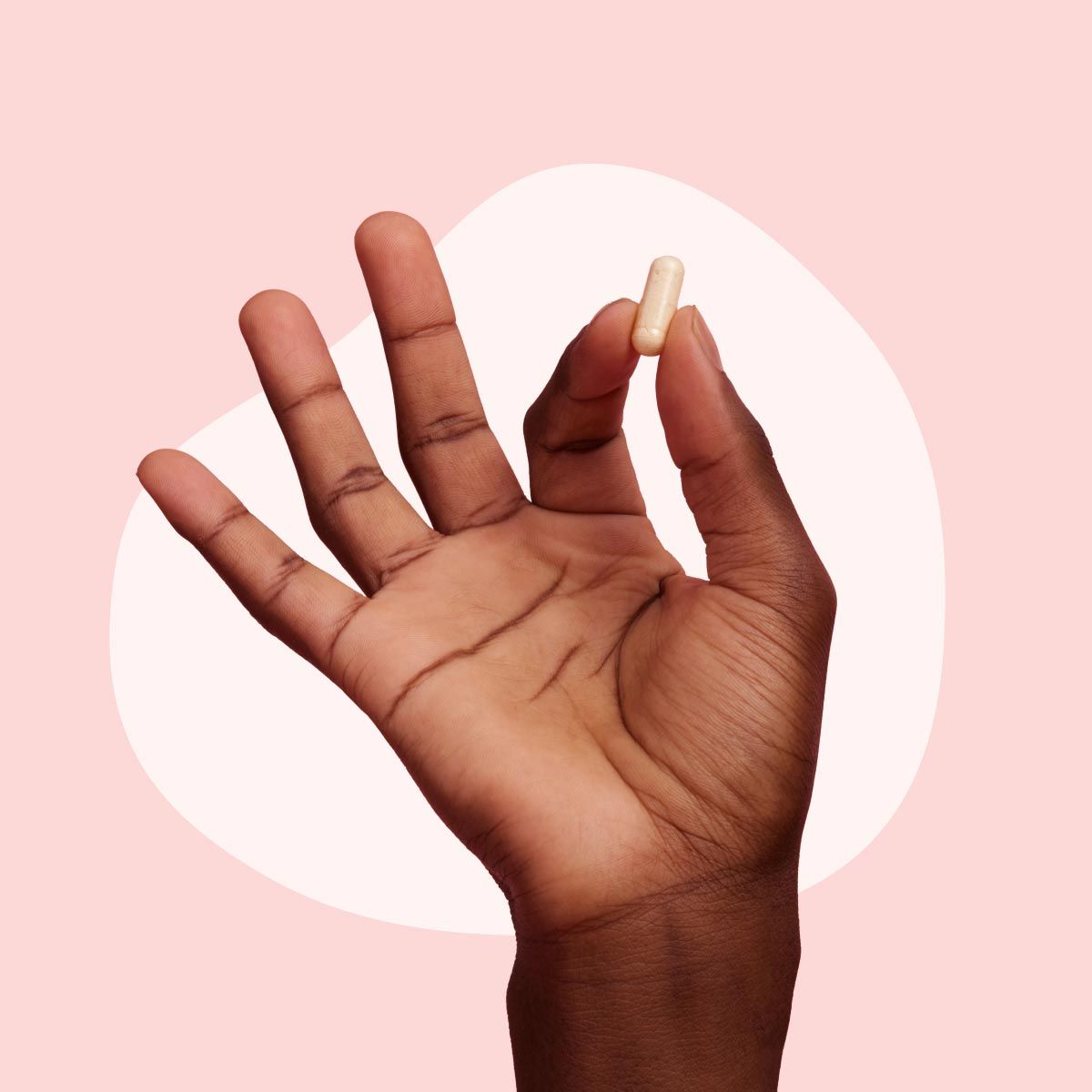A hand holding a Wisp Metabolic Support Capsule on a medium pink background with a lighter pink blob shape behind it.