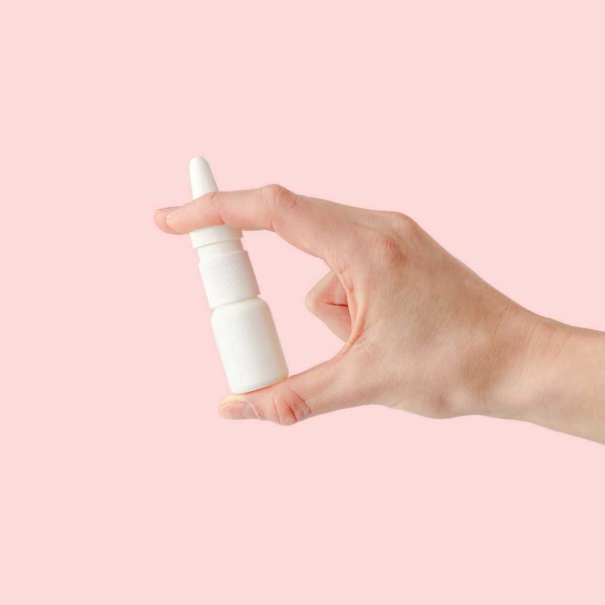 A hand holding a nasal spray bottle in front of a pink background