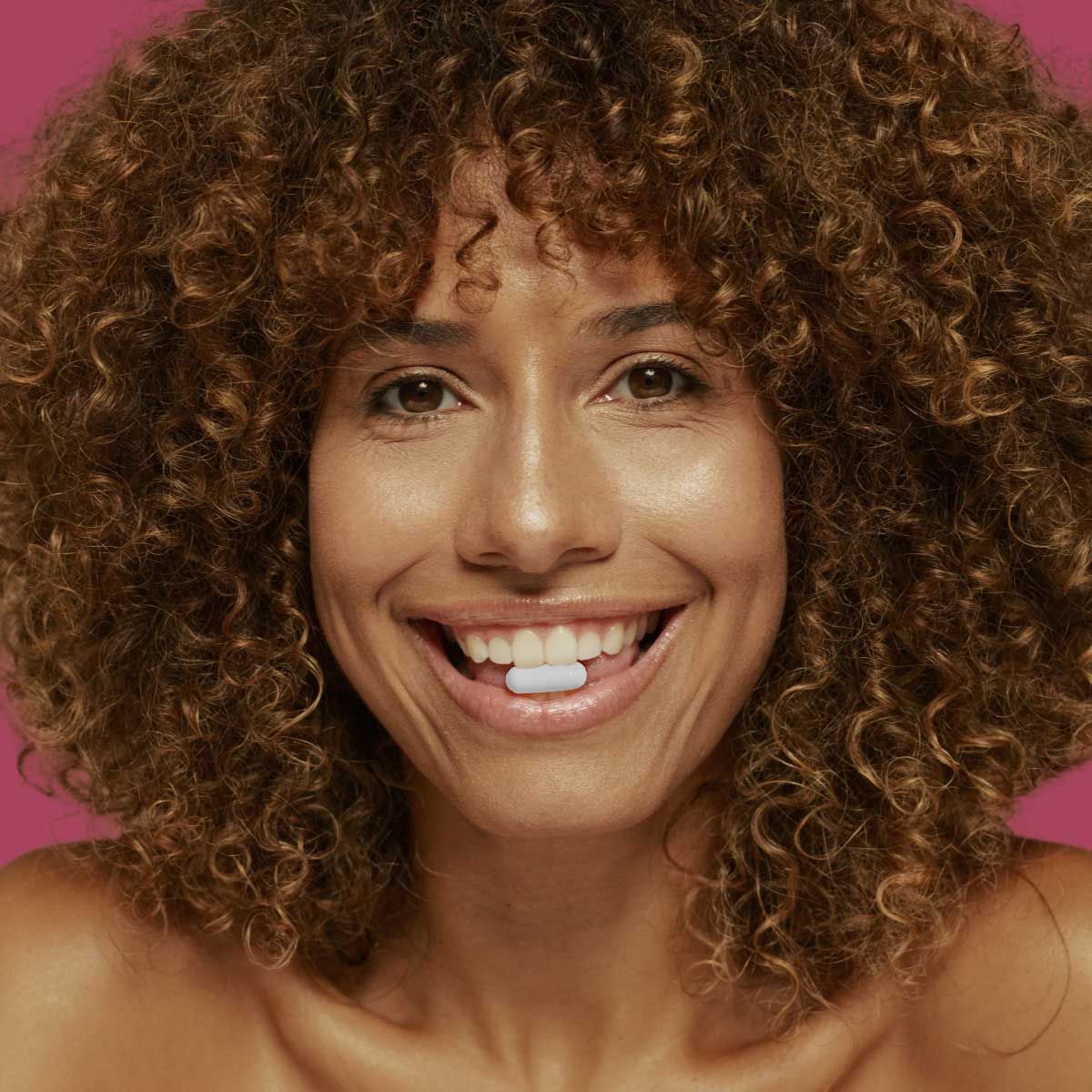 A happy woman with a white capsule between her teeth