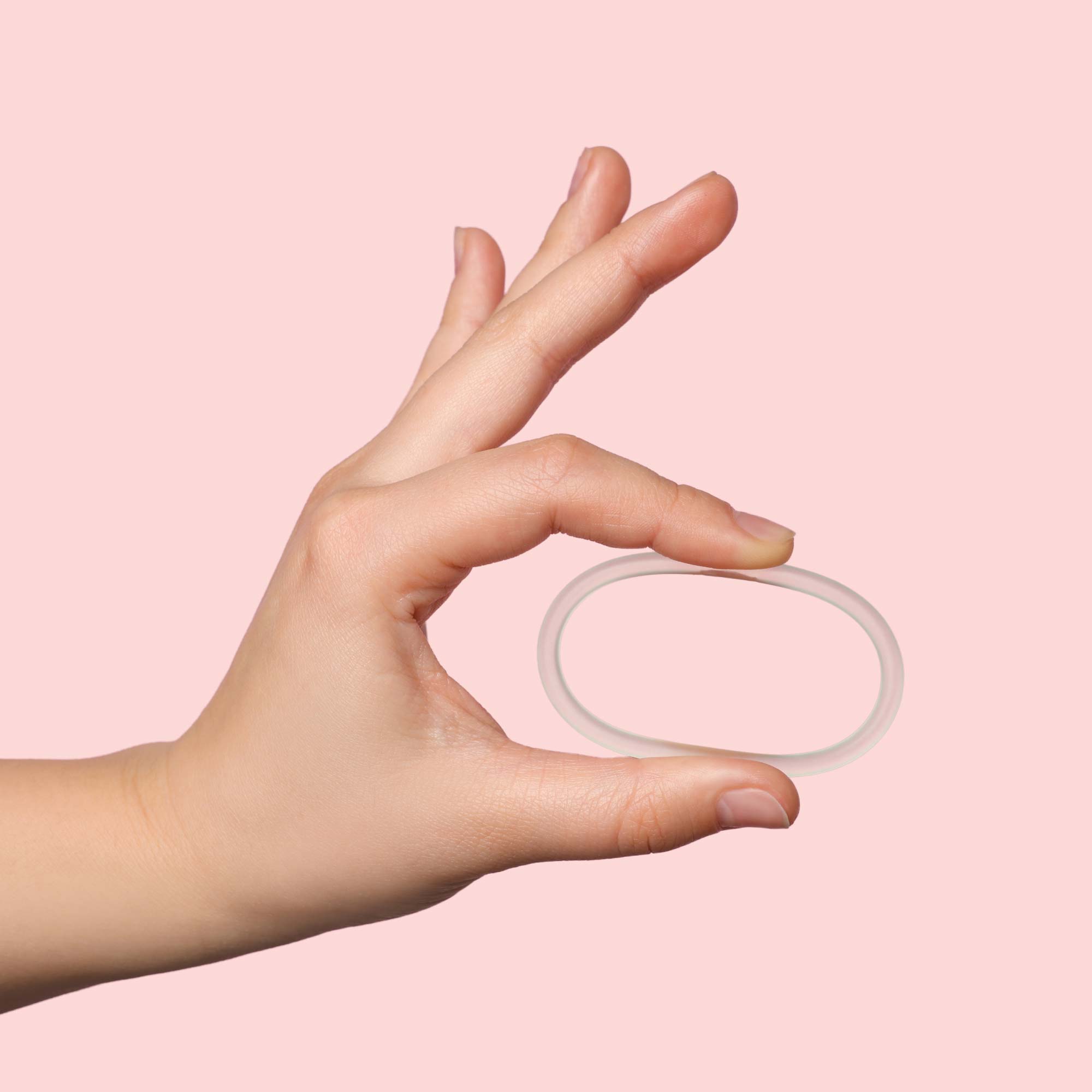 A woman's hand holding NuvaRing in front of a pink background