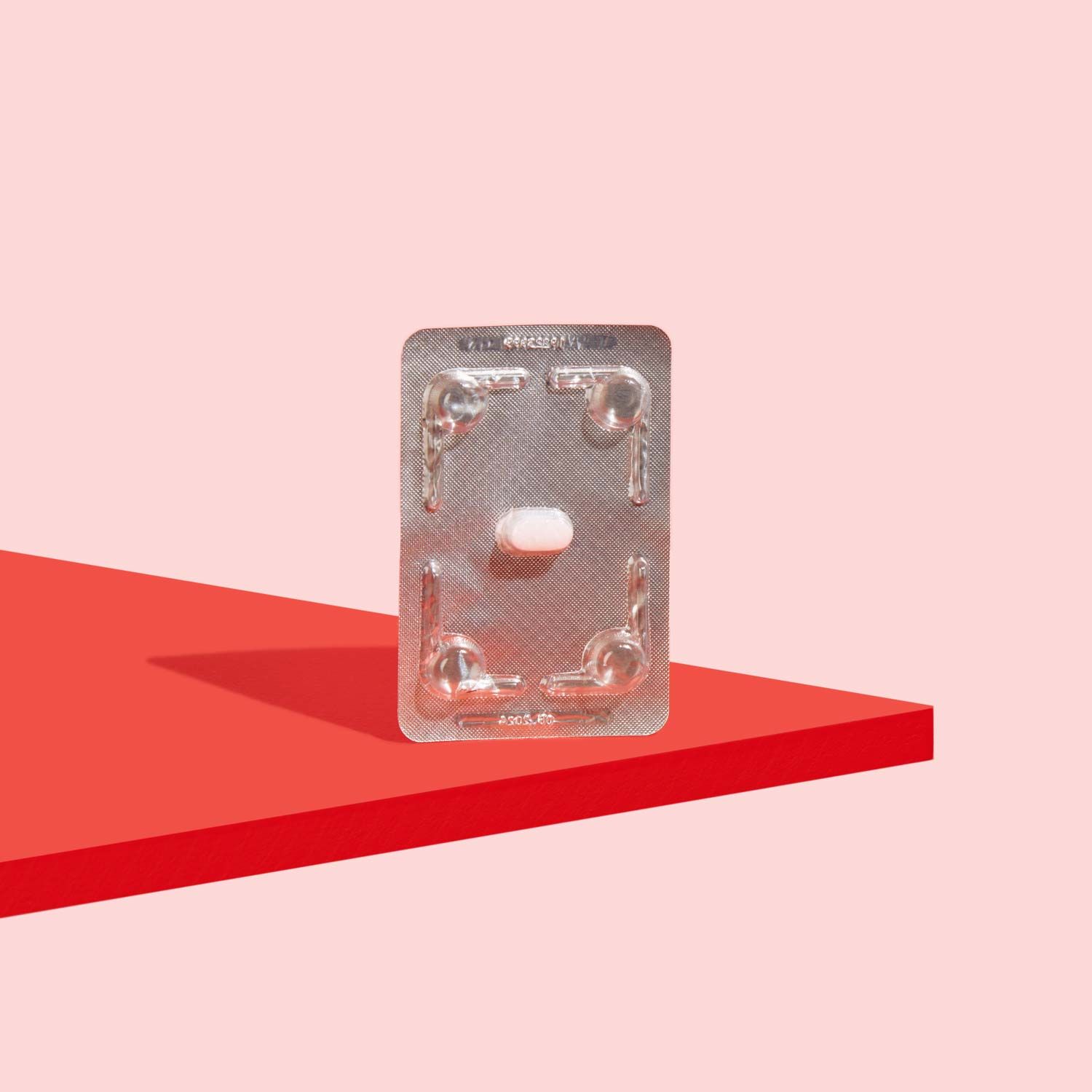A Fluconazole Antifungal pill in a silver foil packet on a red surface with a pink background