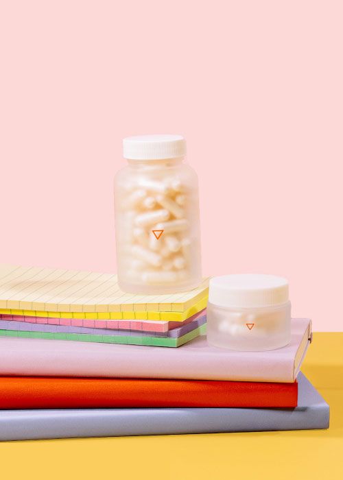 A small and a tall Wisp glass pill jars on colorful notebooks on a yellow surface with a pink background