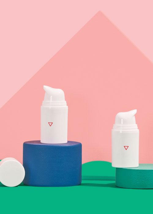 Two Wisp pump bottles balanced on colorful abstract shapes on a green surface with a pink background