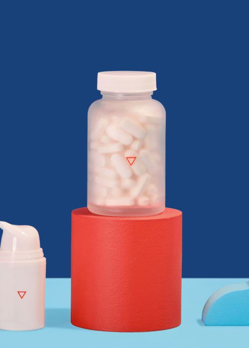 A Wisp tall glass pill jar on a red abstract shape on a light blue surface with a dark blue background