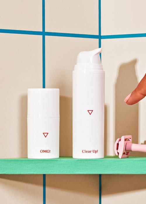 A woman's hand reaching for Wisp Clear Up Acne Cream in the shower on a green shelf with a pink razor