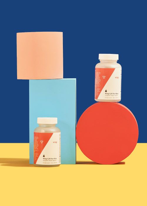 Two bottles of Wisp Lift for Him balanced on colorful abstract shapes on a yellow surface with a dark blue background