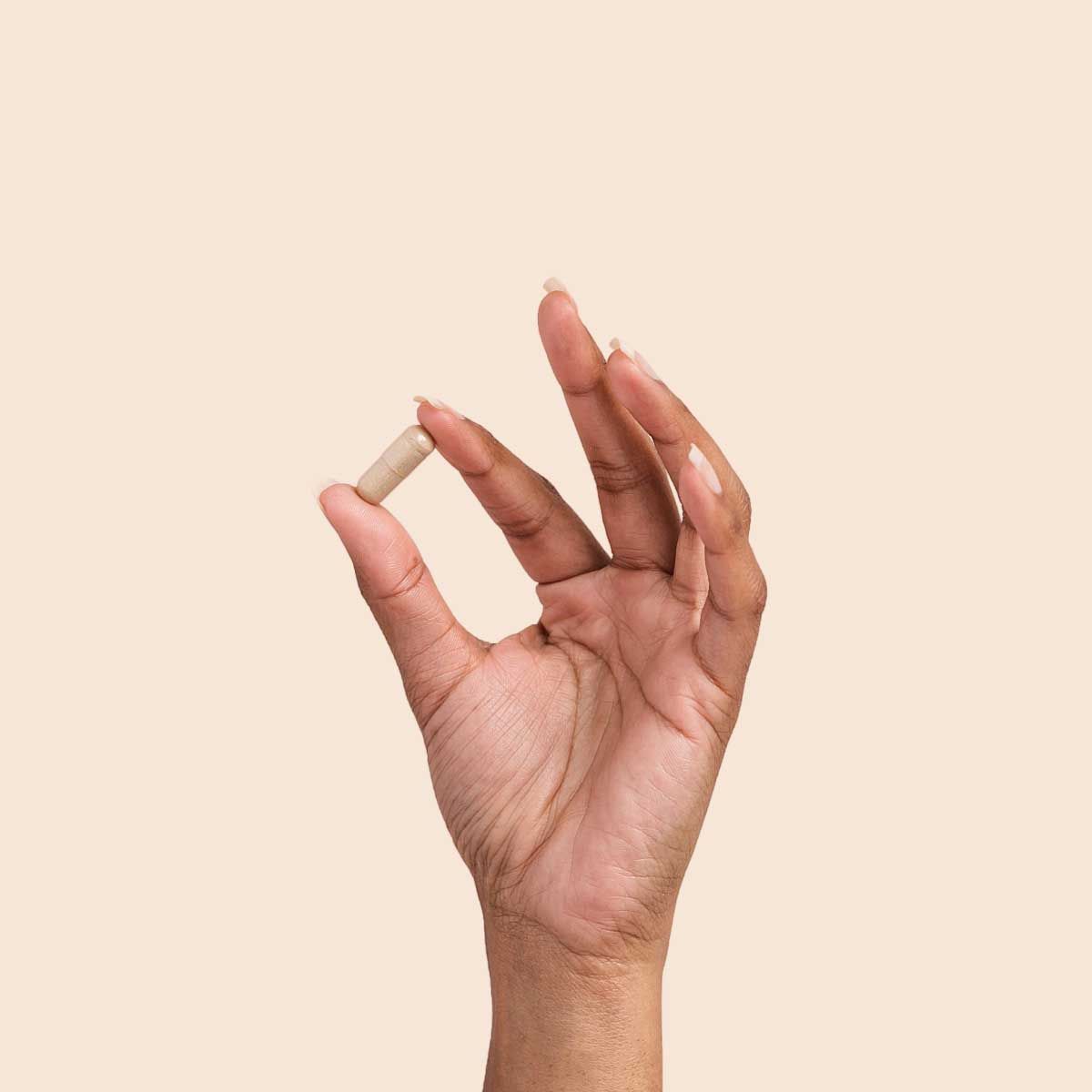 A person's hand holding a pill with a cream background