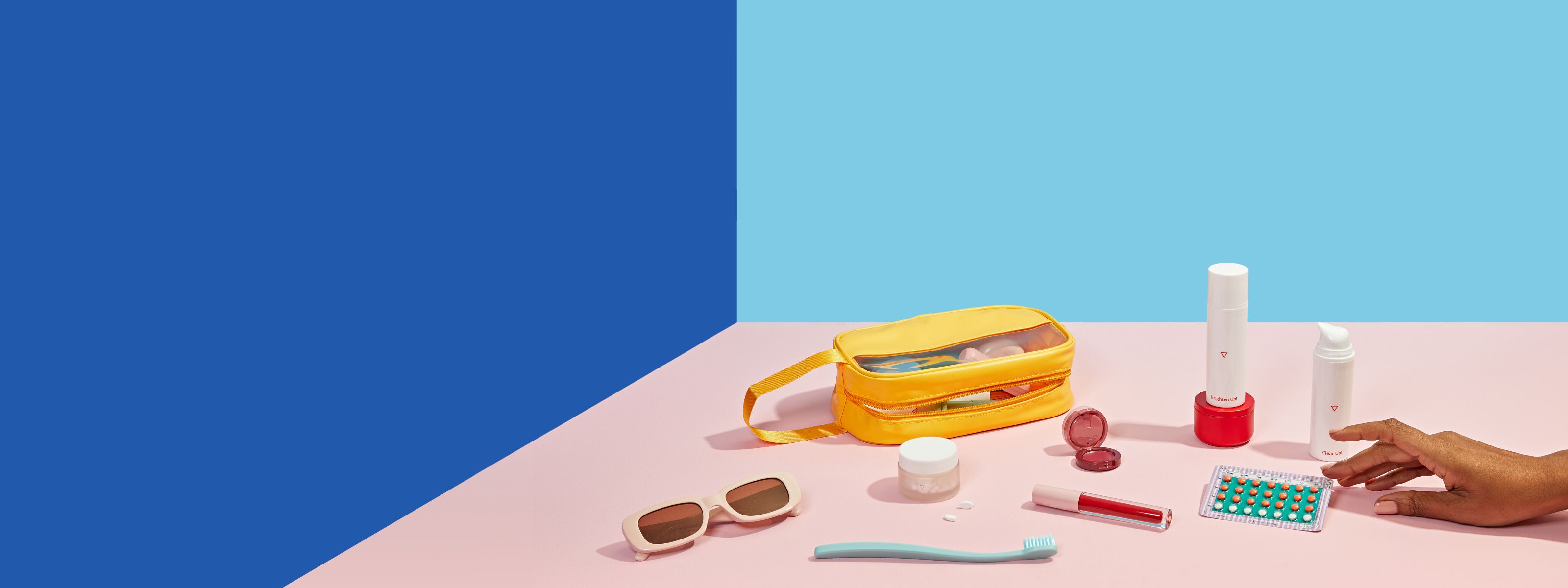 Reproductive health medications from Wisp sit on pink surface with travel bag and toiletries