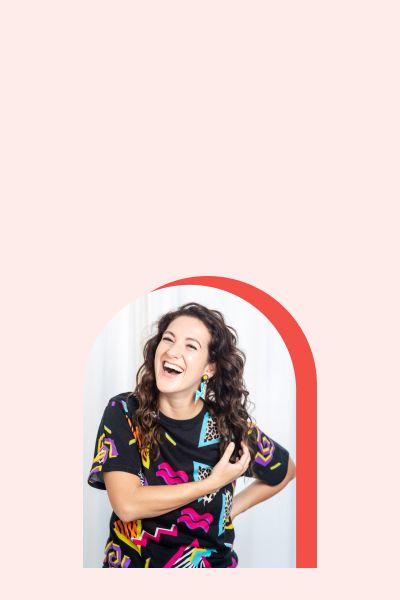 Marlee Liss smiling and wearing a black shirt with colorful abstract shapes on it in front of a light pink background