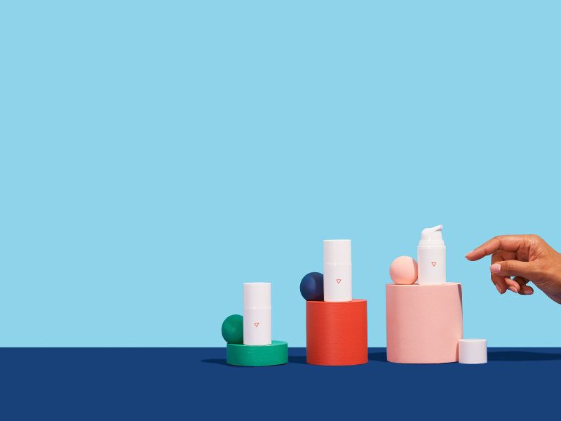 Two bottles of Wisp Hydrocortisone cream balanced on colorful abstract shapes on a blue surface