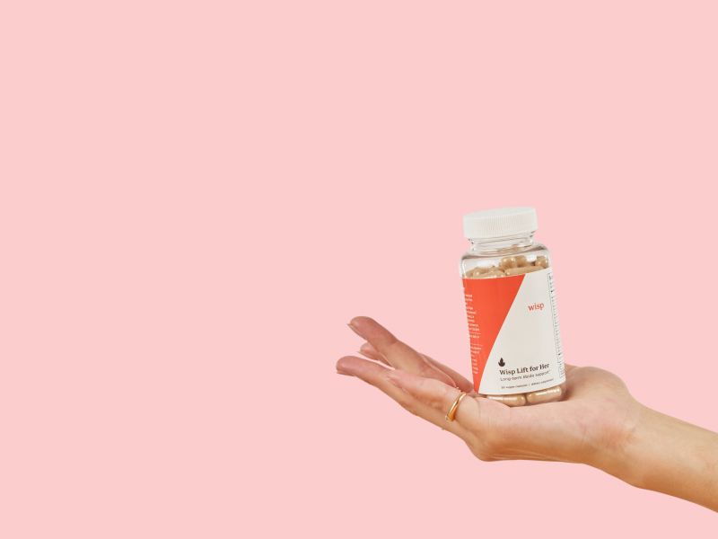 Woman's hand holding Wisp Lift for Her Libido Supplements on a pink background