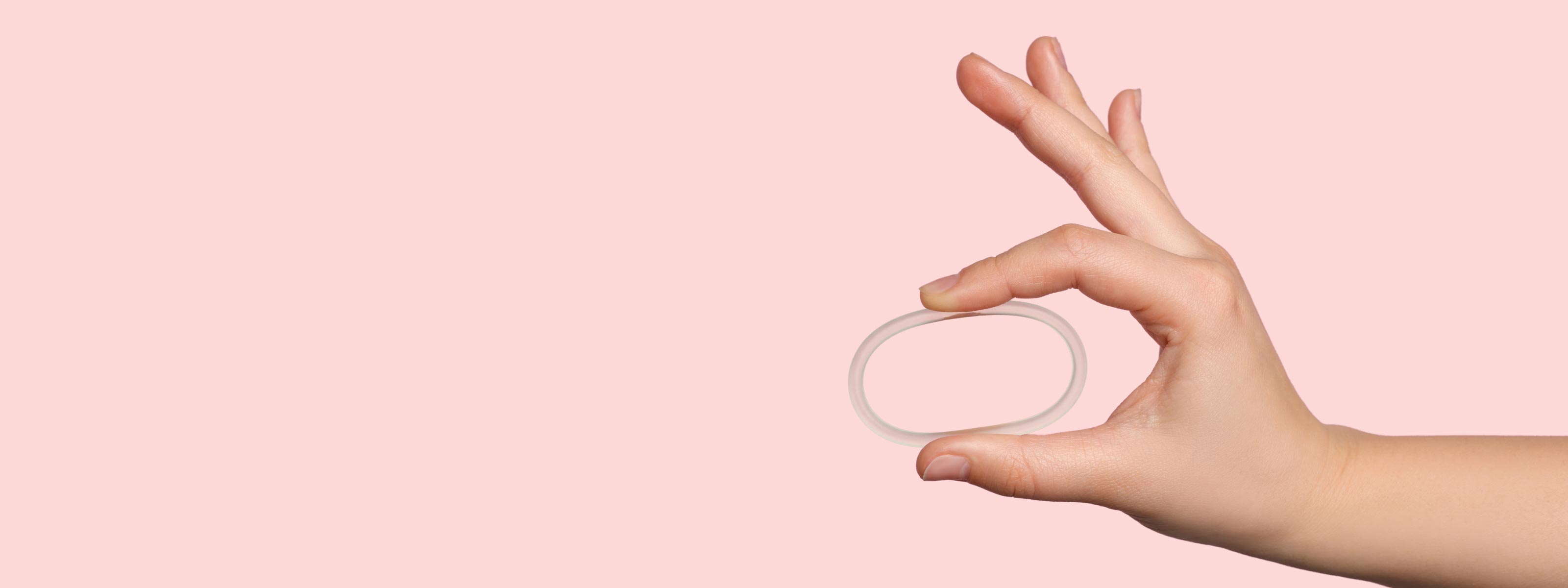 Woman's hand holding NuvaRing Birth Control with a pink background