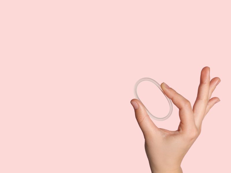 Woman's hand holding NuvaRing Birth Control with a pink background